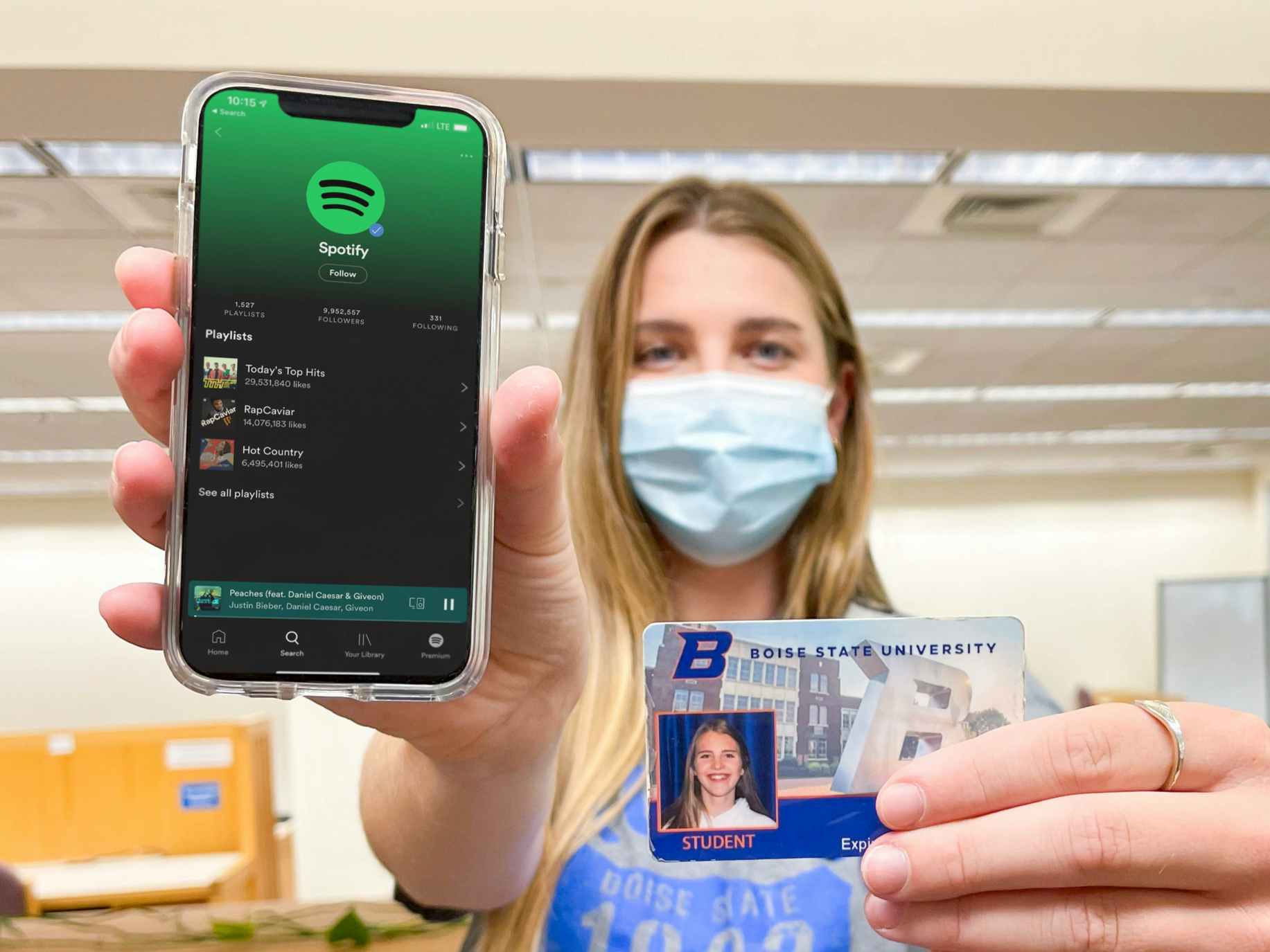 A college student holding out cell phone with Spotify open with one hand and her student ID with the other hand.