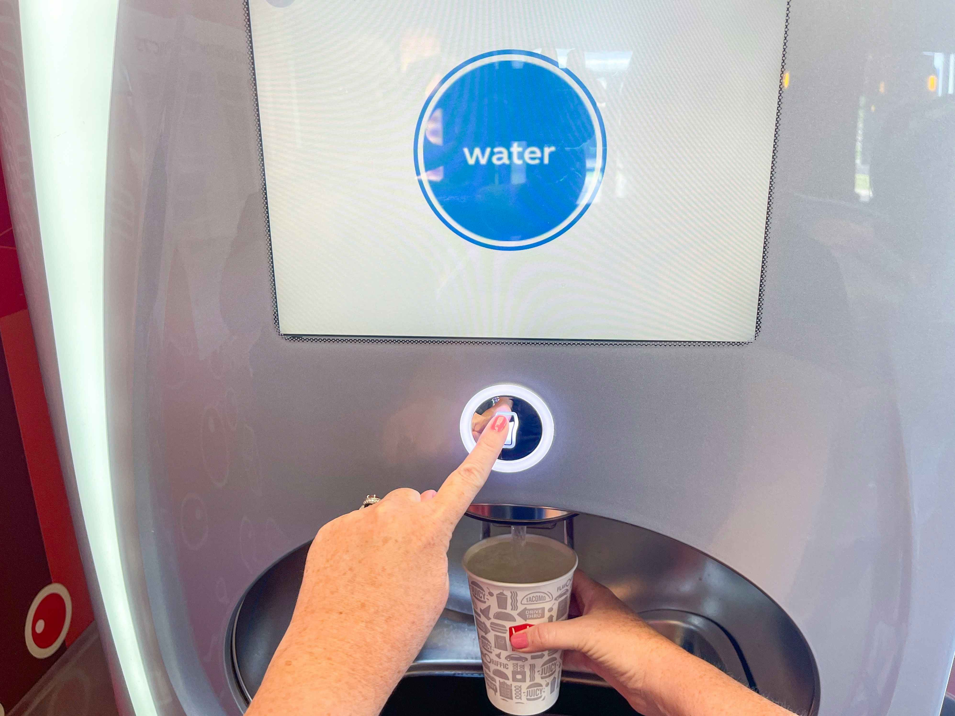 a person filling up a fast food cup with water from soda machine