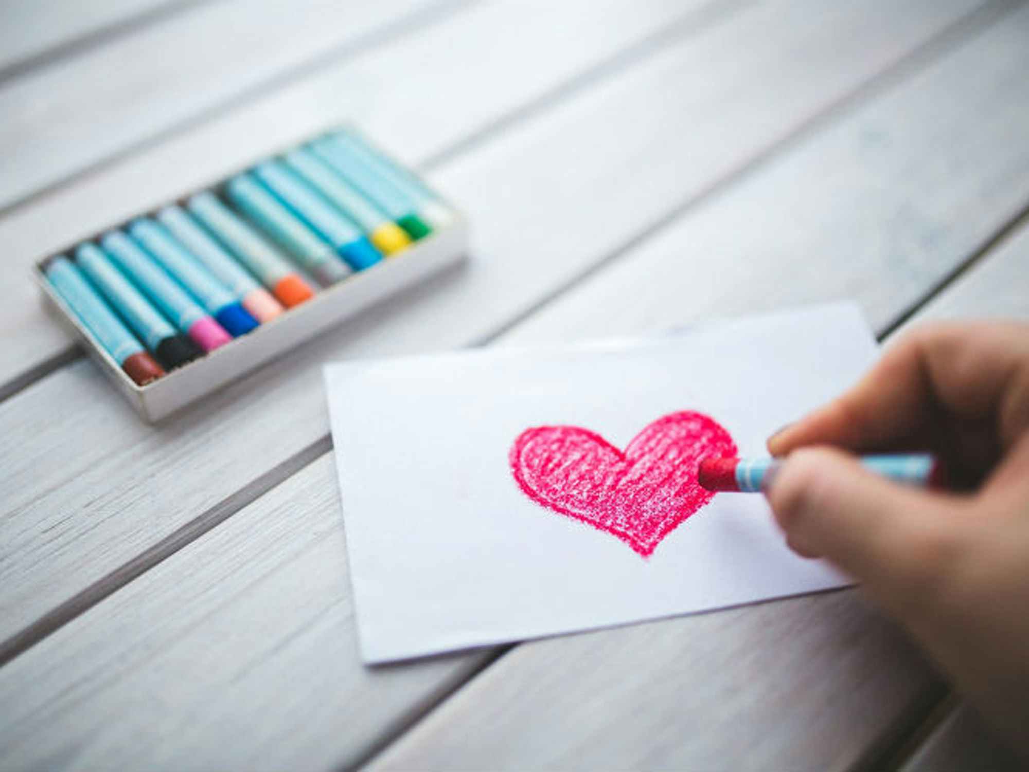someone coloring a heart shape onto a piece of paper with a crayon