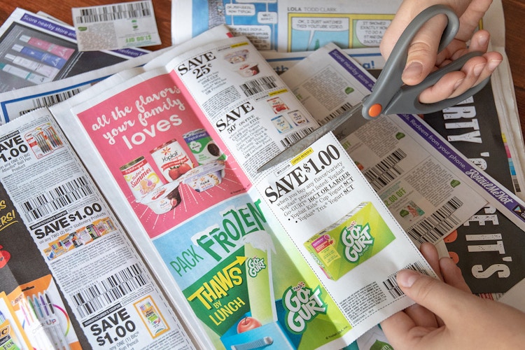 Person using scissors to cut a $1.00 coupon for Yoplait Go-Gurt