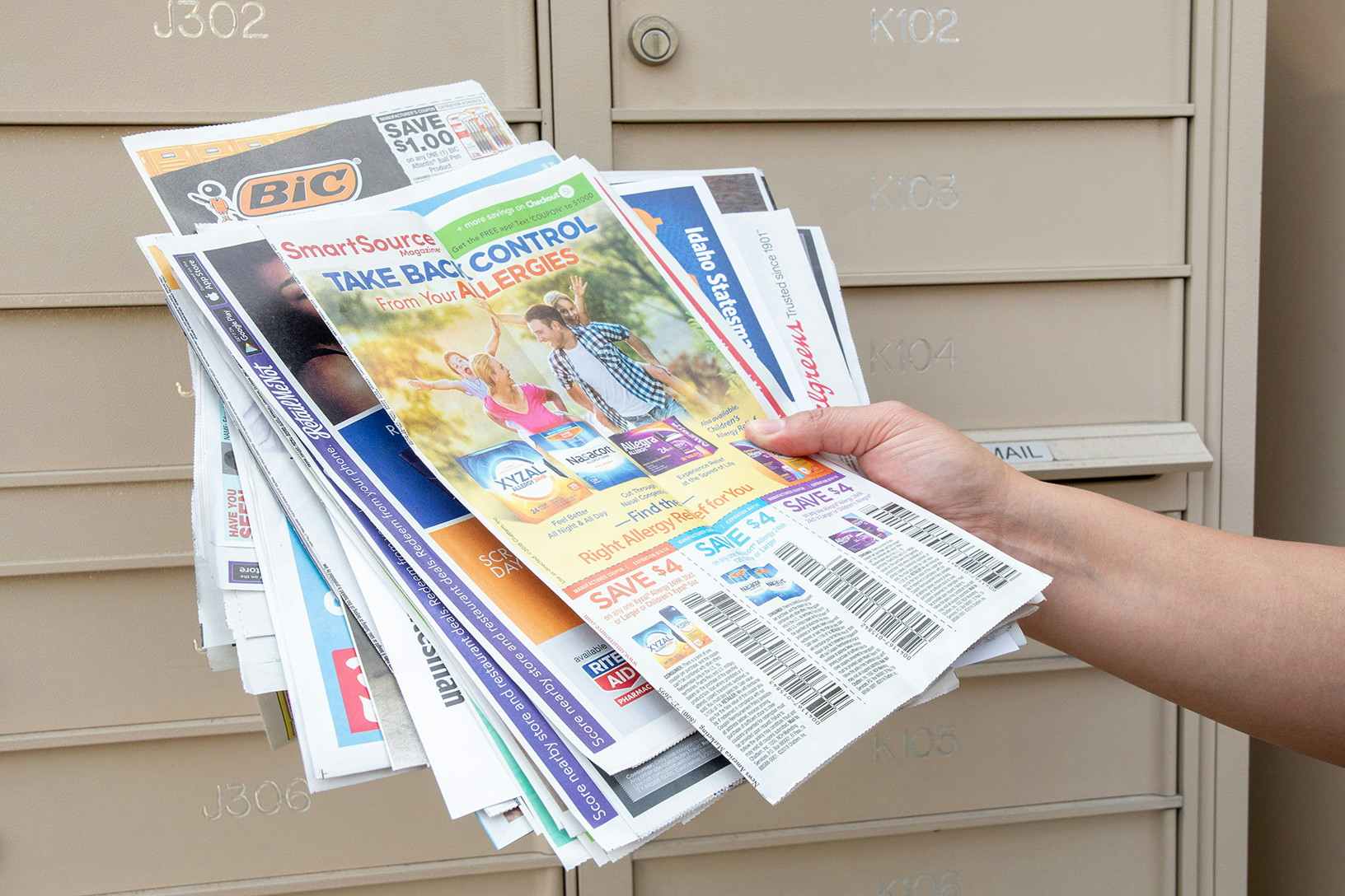 woman holding a bunch of newspaper inserts near a community mailbox area