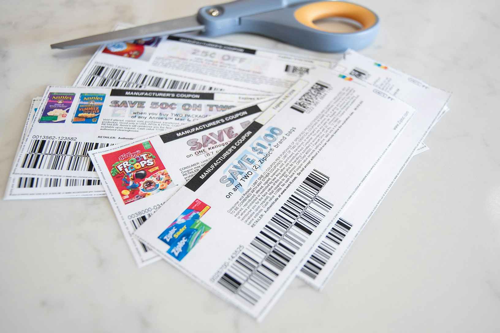 A pile of printed coupons laying on a counter next to a pair of scissors.