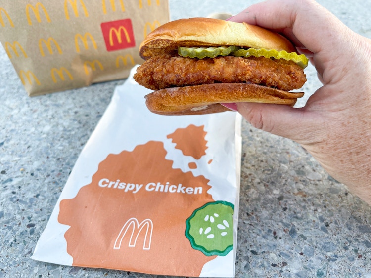 a person holding a mcdonlds crispy chicken sandwich infront of wrapper and to go bag