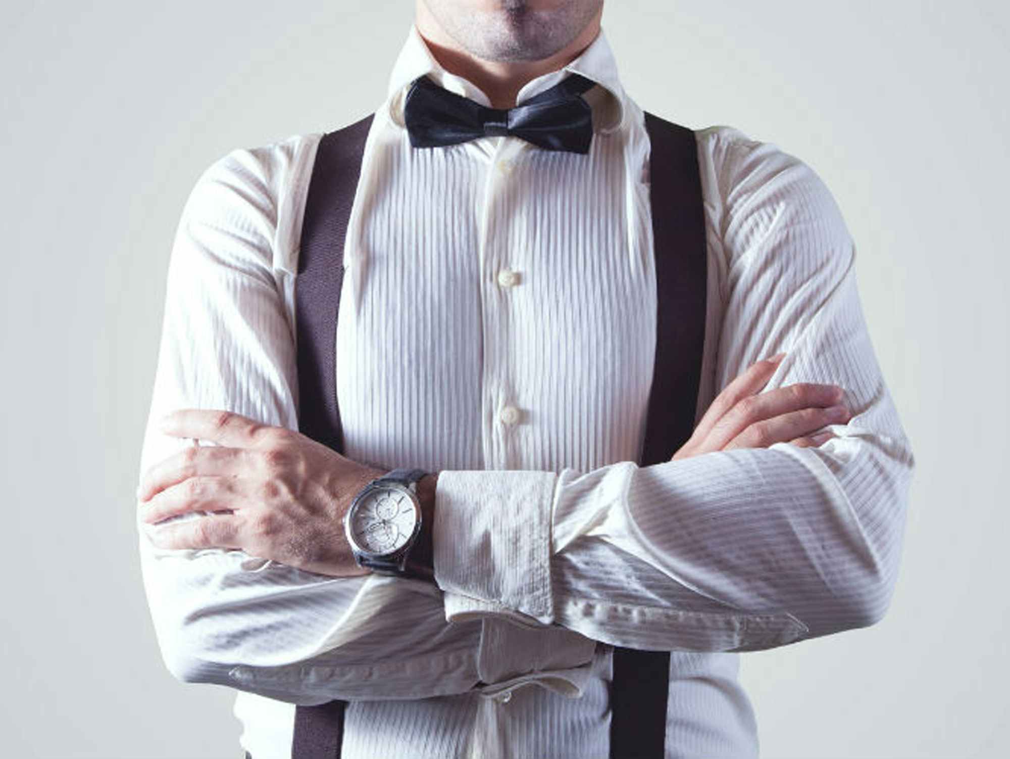 a person crossing their arms wearing suspenders and a bow tie
