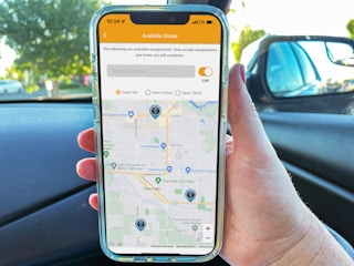 a person holding a cellphone with mystery shopper map on screen while person sitting in car
