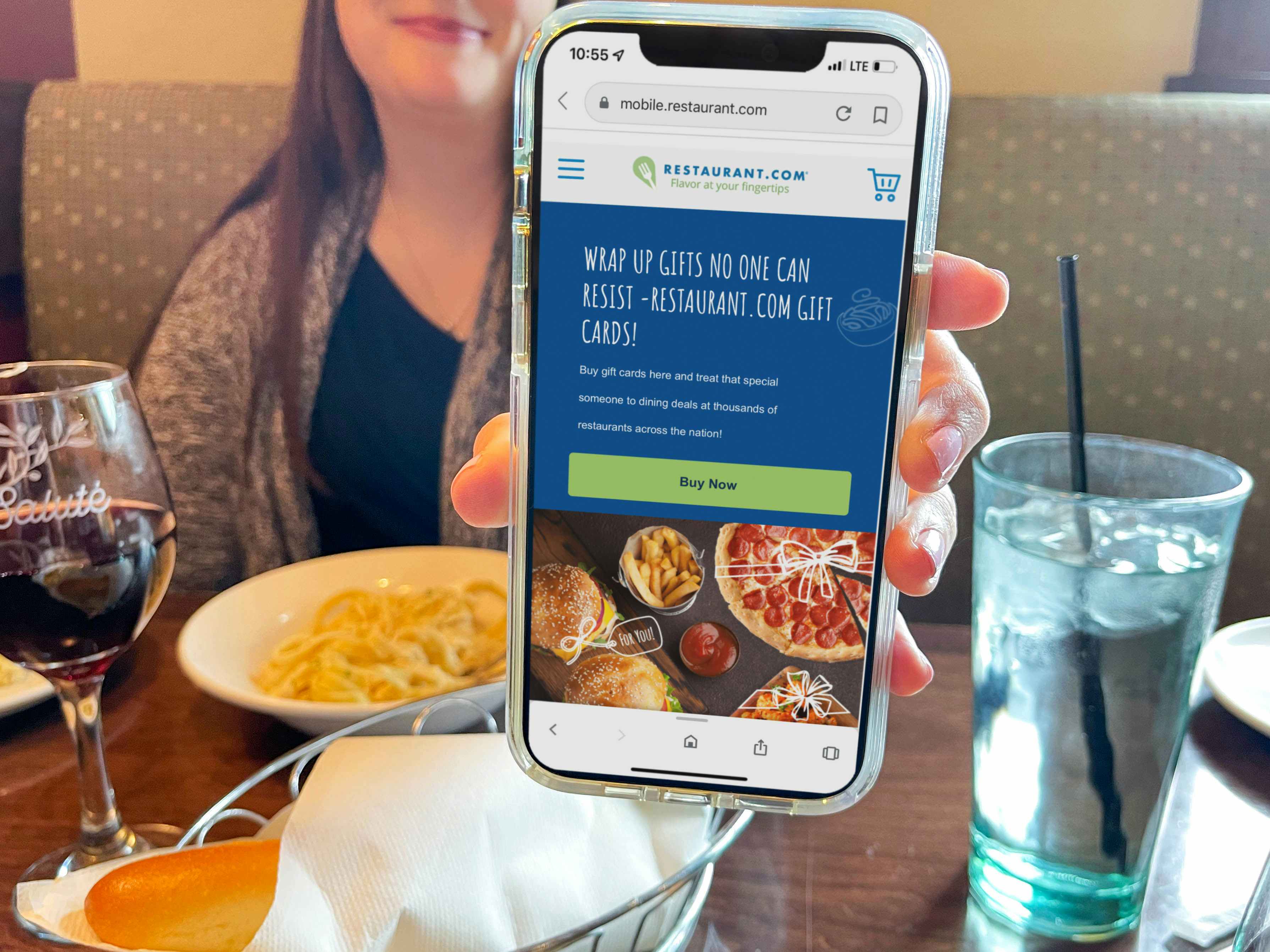 a woman at table in olive garden holding a cellphone with restaurant website on screen