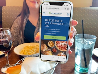 a woman at table in olive garden holding a cellphone with restaurant website on screen