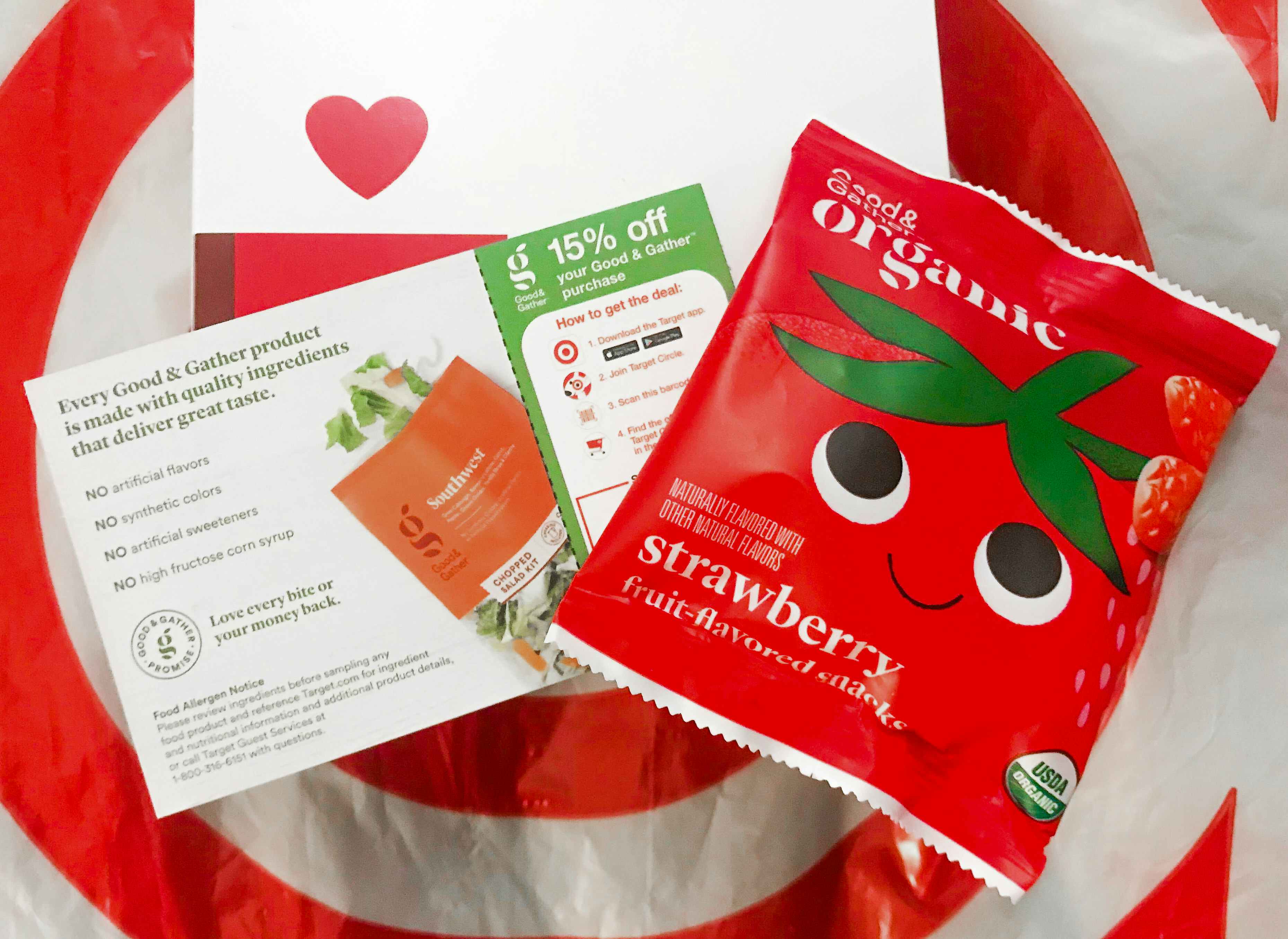 A target good and gather coupon for 15% off next to a free sample of Good & Gather strawberry fruit snacks on top of a Target plastic bag