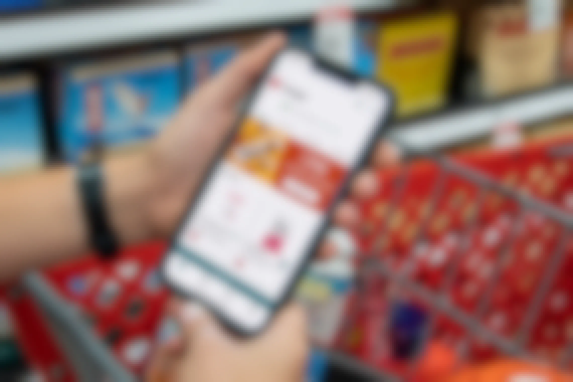 A person's hands resting on a Target shopping cart handle holding an iPhone that is displaying the Ibotta mobile app offers for Target.