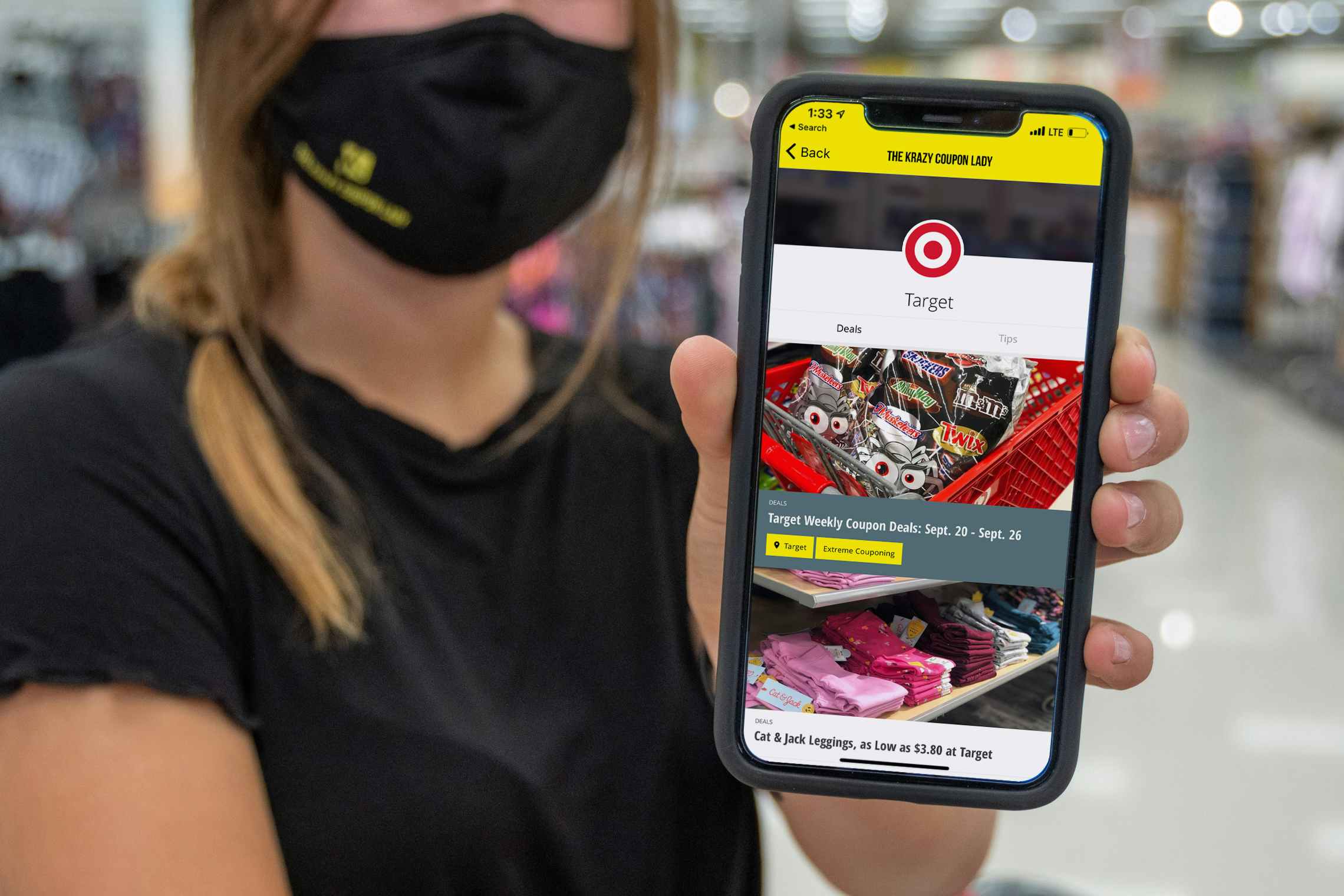 A woman wearing a mask, holding up a phone with the KCL mobile app displayed on it.