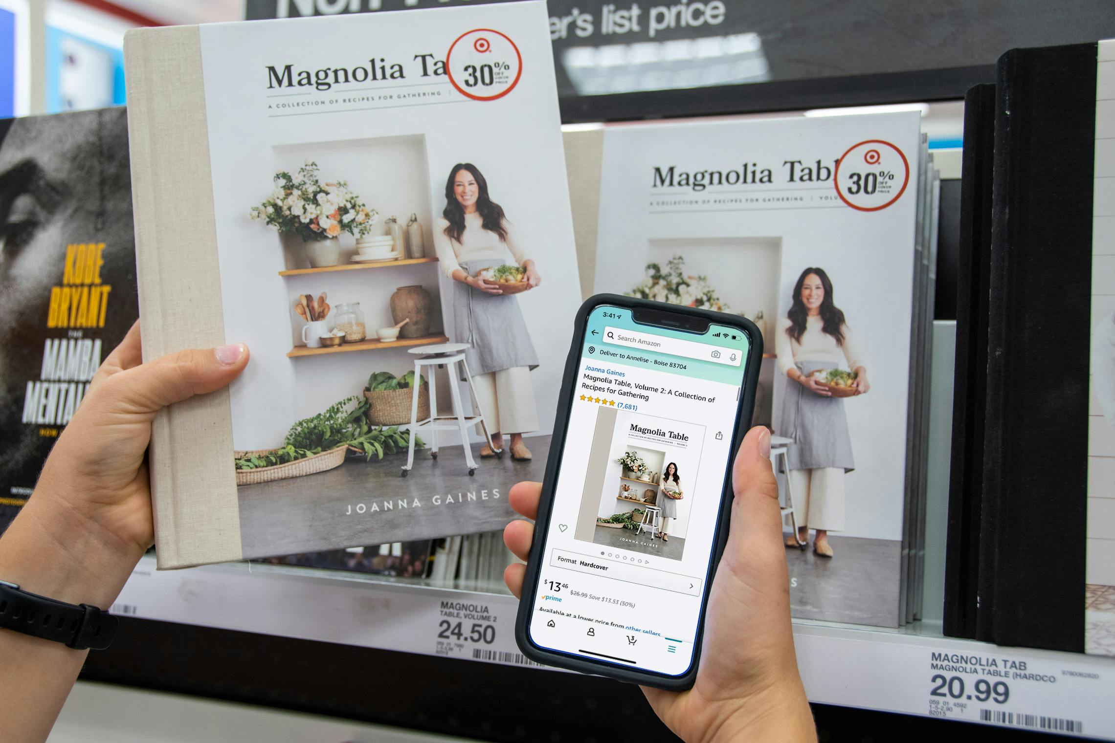 A person holding a copy of Magnolia Table next to a cell phone displaying a lower price for the book on the Amazon app.