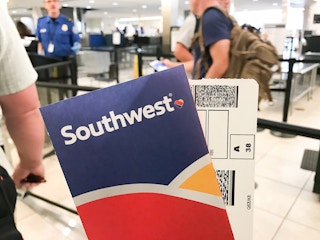 A Southwest airline ticket and envelope being held up while people are standing in line for TSA.
