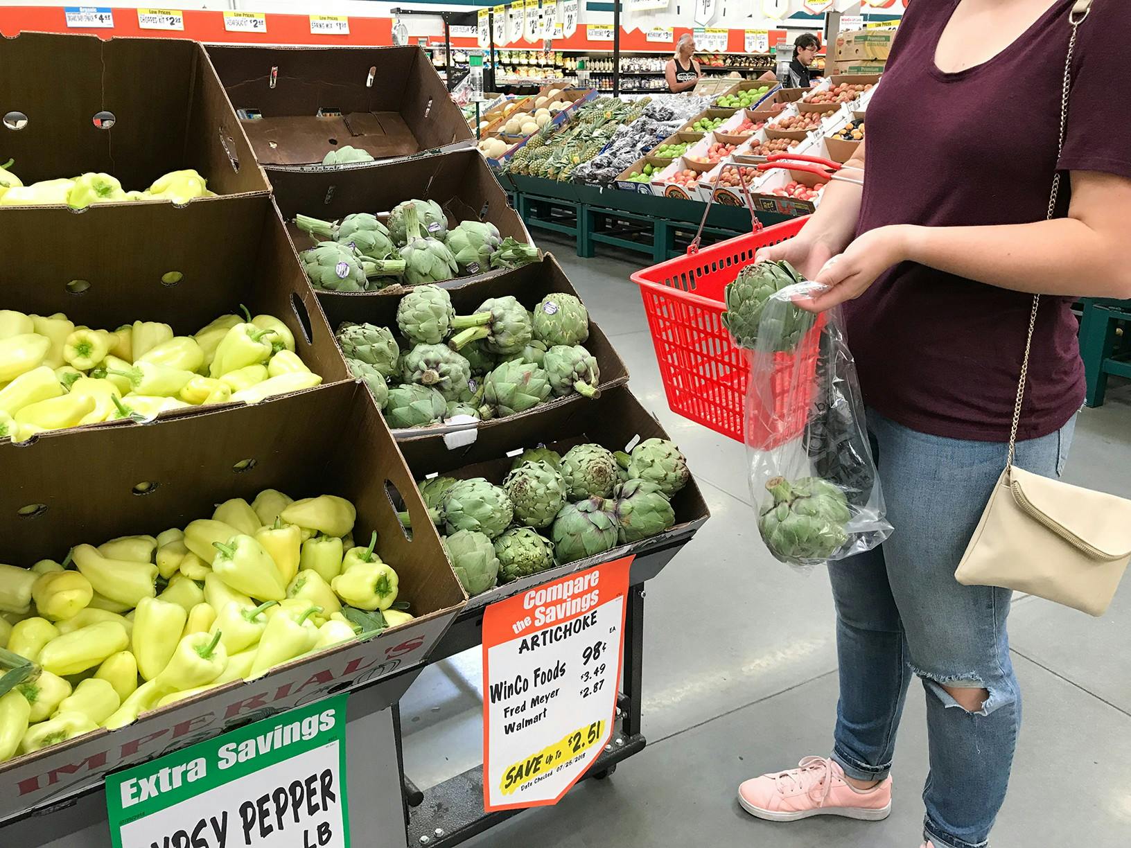 A woman picking out artichikes and placing them in a plastic bag.