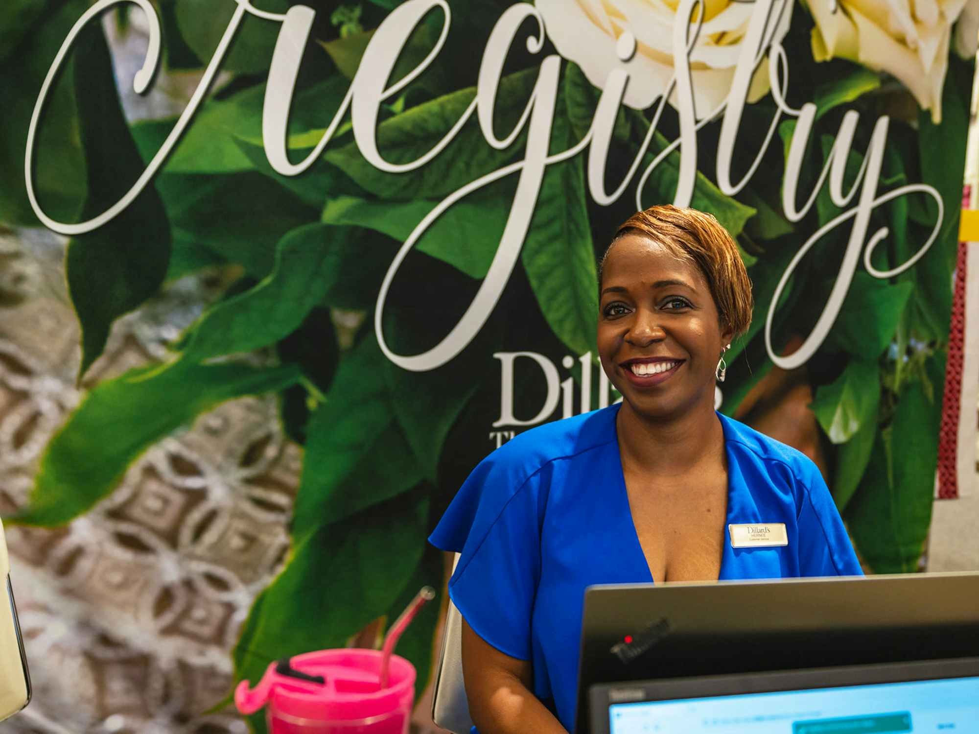 A Dillard's employee smiling and standing at the Registry counter inside Dillard's
