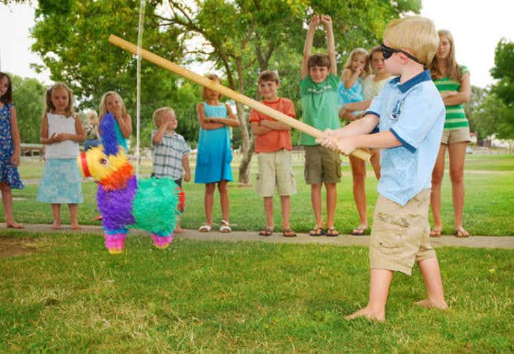 A blindfolded child with a stick going to hit a piñata while other children watch.