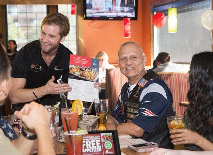 An Applebee's employee showing the menu to a table of patrons. There are several drinks on the table in front of the patrons.