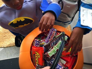 Two boys dressed in costumes reaching into a plastic pumpkin filled with candy.