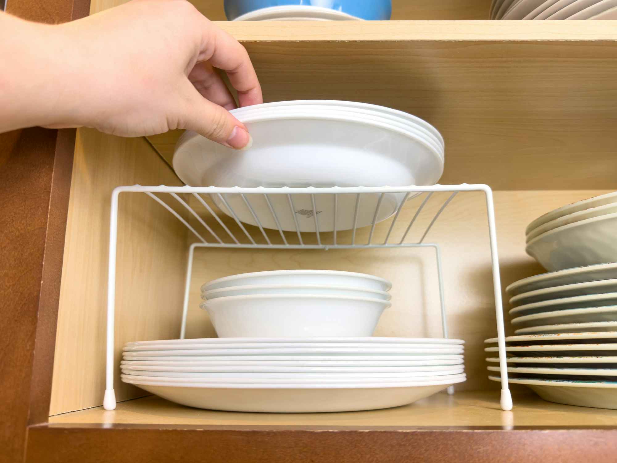 Someone putting dishes onto a small shelf inside a kitchen cabinet