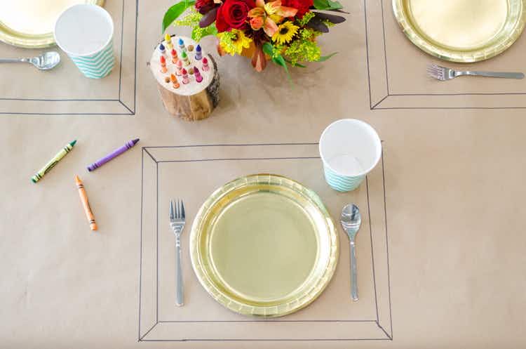 A place setting drawn onto a paper tablecloth with crayons next to the dinnerware.