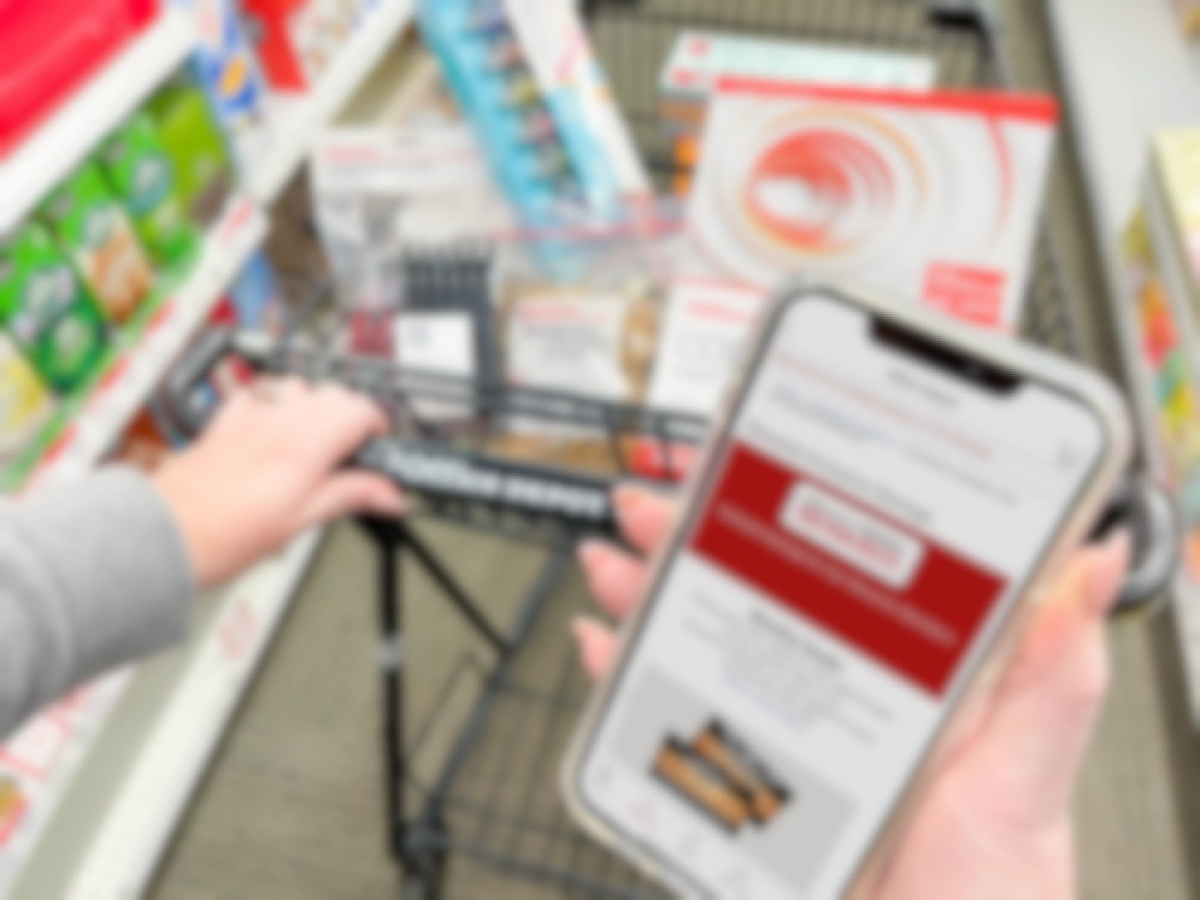 A person's hand holding an iPhone that is displaying the Office Depot mobile app's Rewards page. In the background, the person's other hand is pushing an Office Depot shopping cart full of office supplies down an aisle at Office Depot.