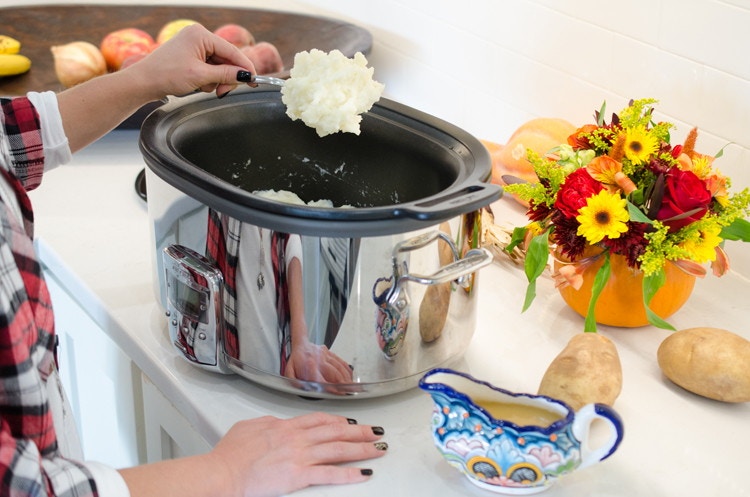 Someone spooning mashed potatoes out of a slow cooker.