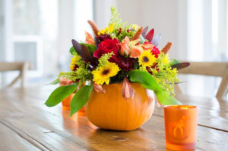 A centerpiece made from a small pumpkin and autumn flowers.