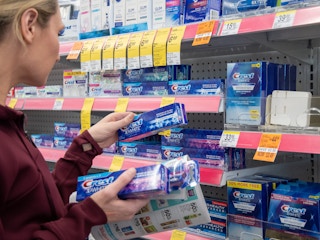 A woman grabbing toothpaste from a walgreen's store shelf with an ad in hand