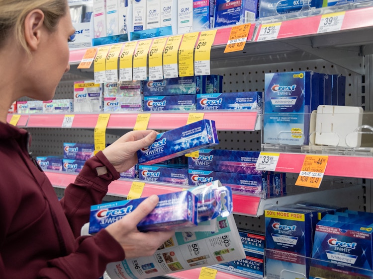 A woman grabbing toothpaste from a walgreen's store shelf with an ad in hand