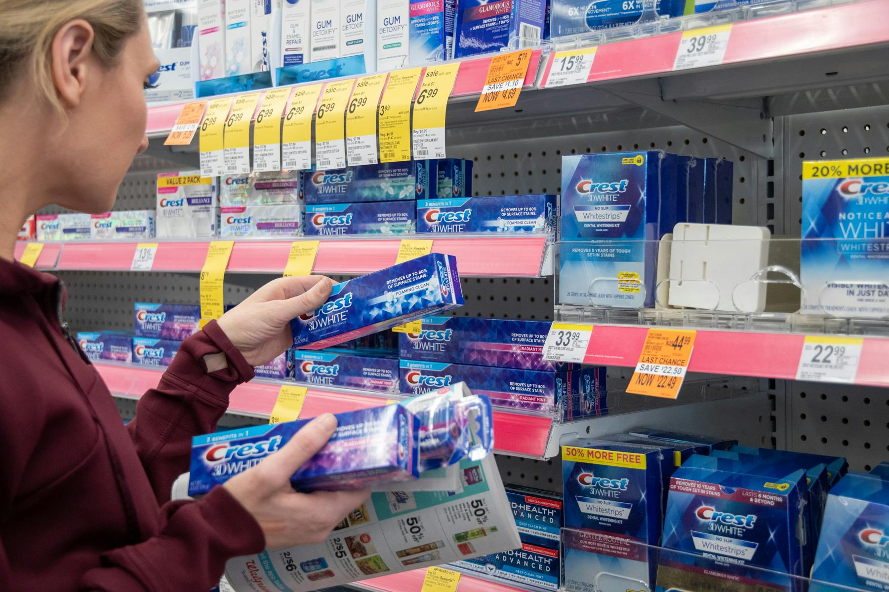 A woman grabbing toothpaste from a walgreen's store shelf with an ad in hand