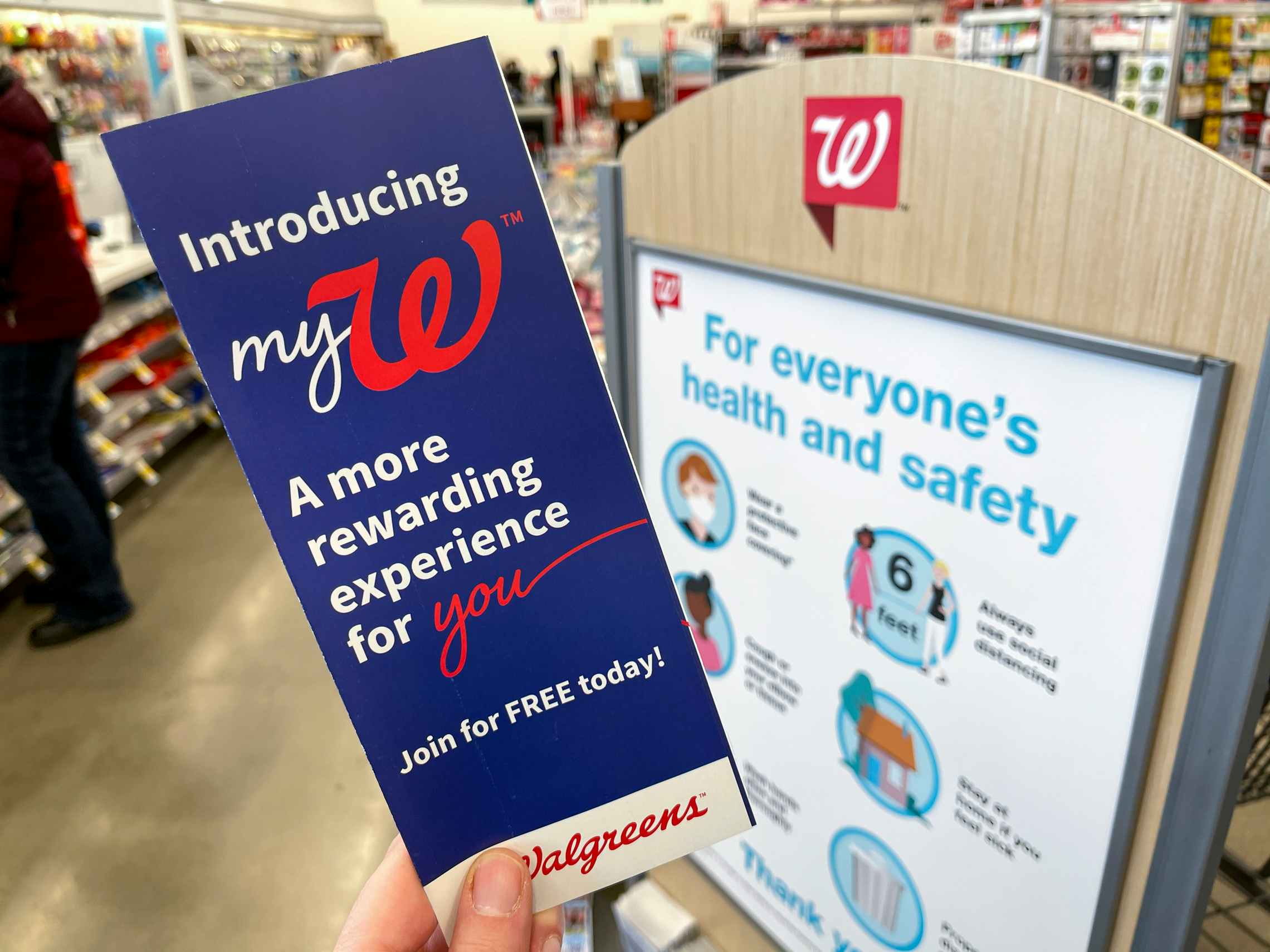 A person's hand holding a mywalgreens rewards pamphlet in front of a Walgreens sign.