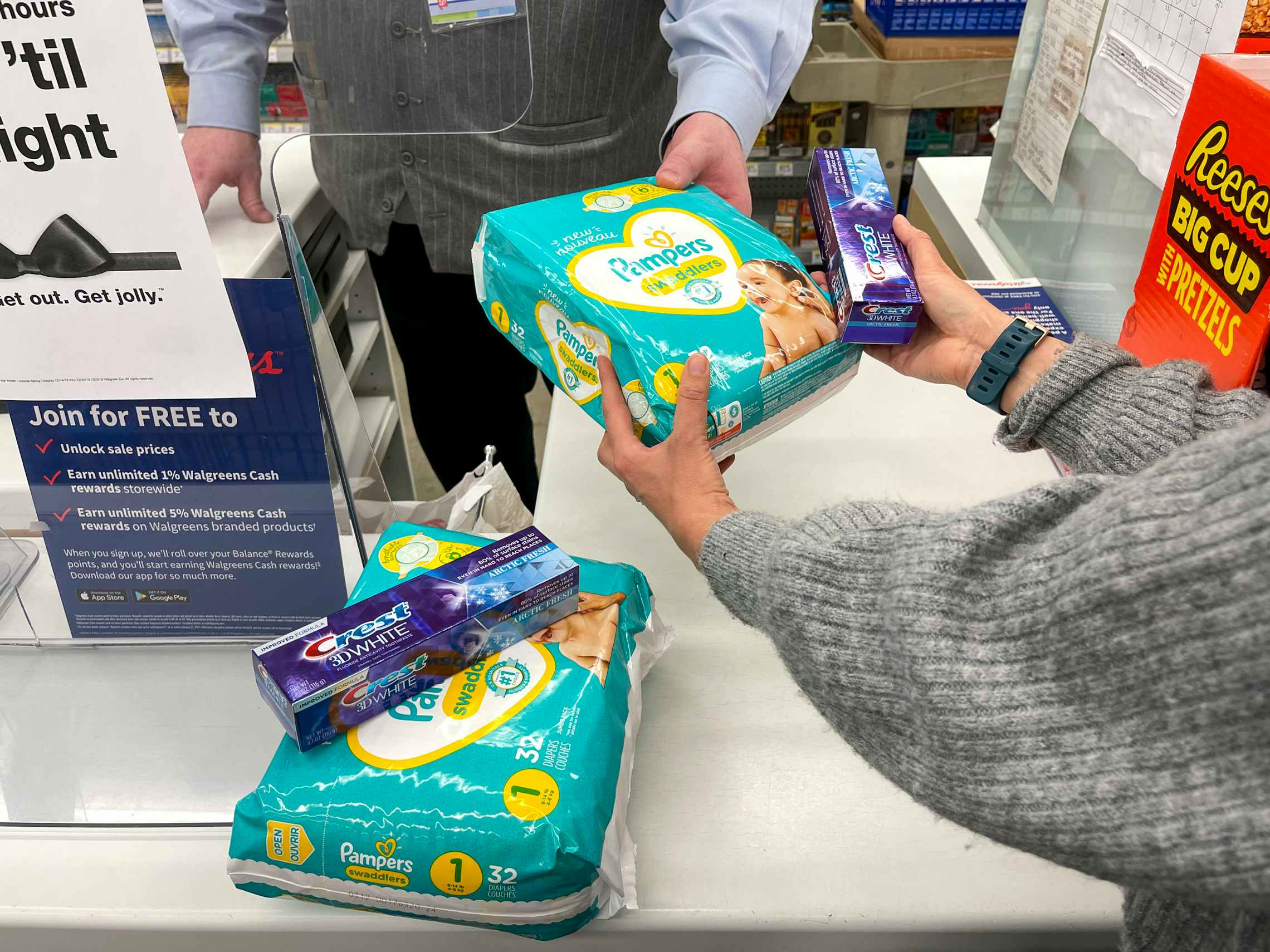 A woman handing a pack of pampers diapers and crest to a casher with a second pack of diapers and crest on the counter.