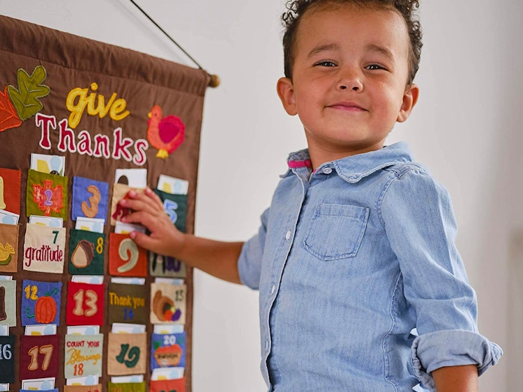 A little boy standing next to a Thanksgiving advent calendar hanging on the wall.