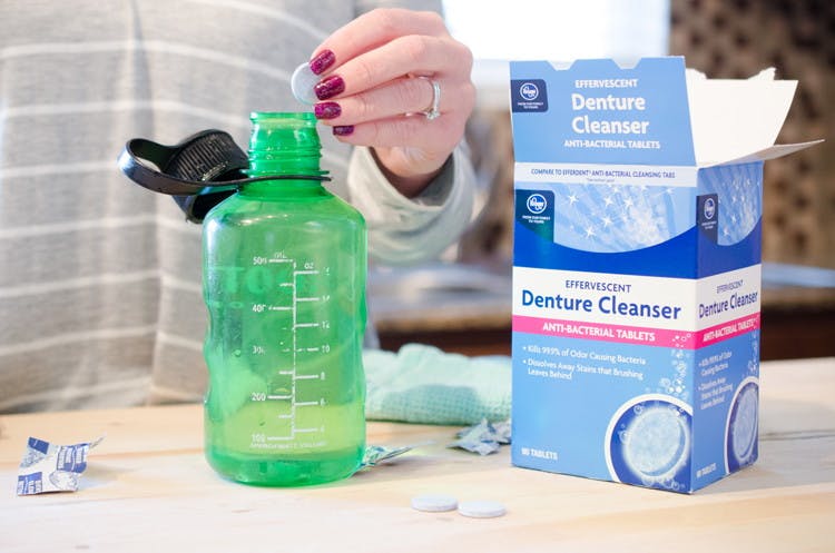 A woman dropping a denture tablet into an empty plastic water bottle.
