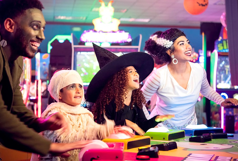 A family wearing Halloween costumes playing an arcade game at Chuck E Cheese