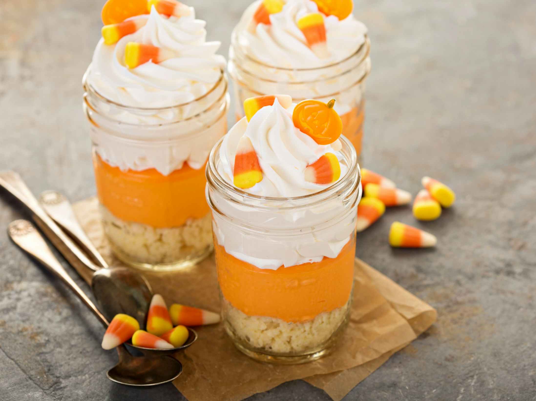 Three jars filled with candy corn parfaits with candy corn on the table.