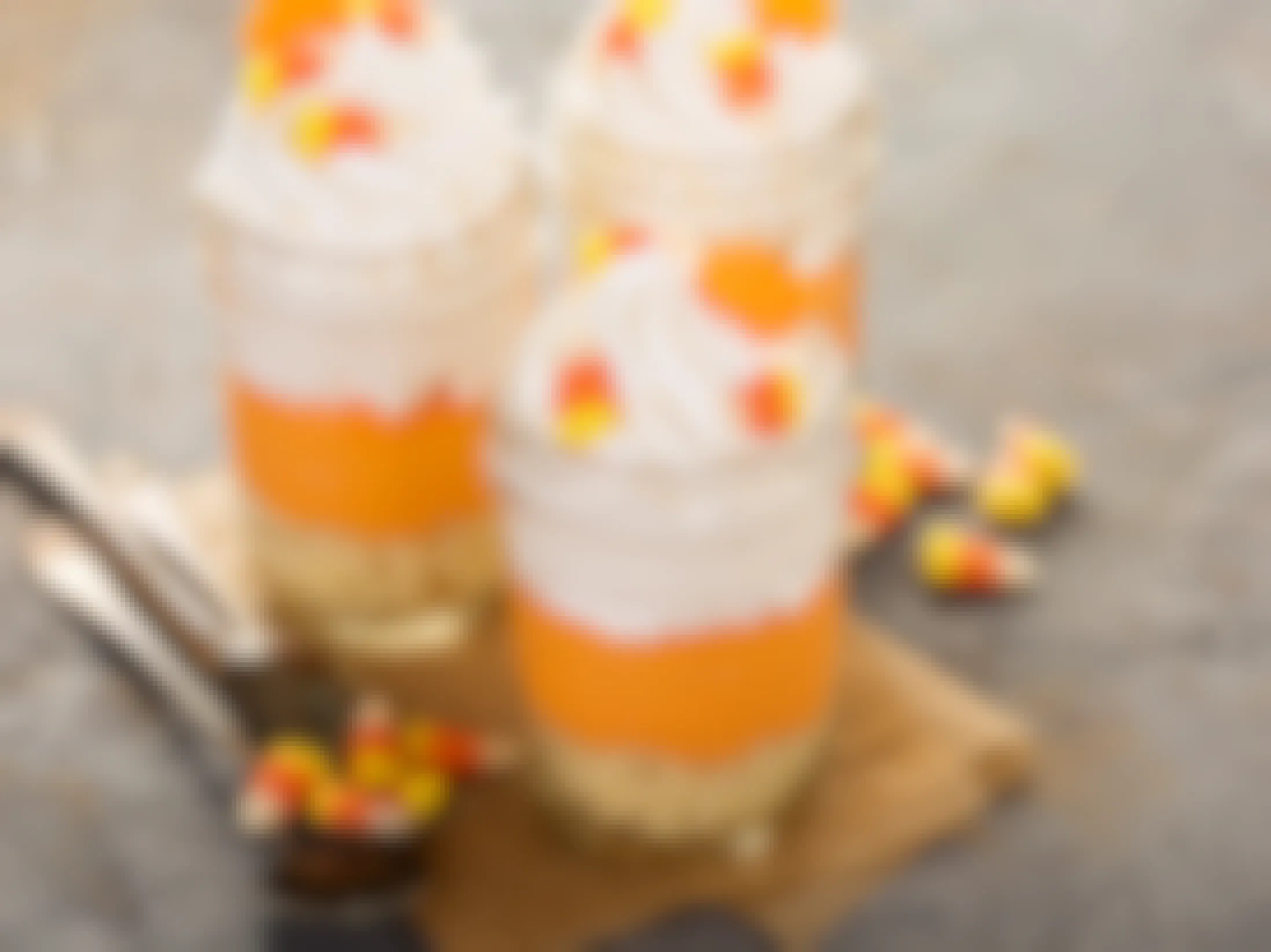 Three jars filled with candy corn parfaits with candy corn on the table.