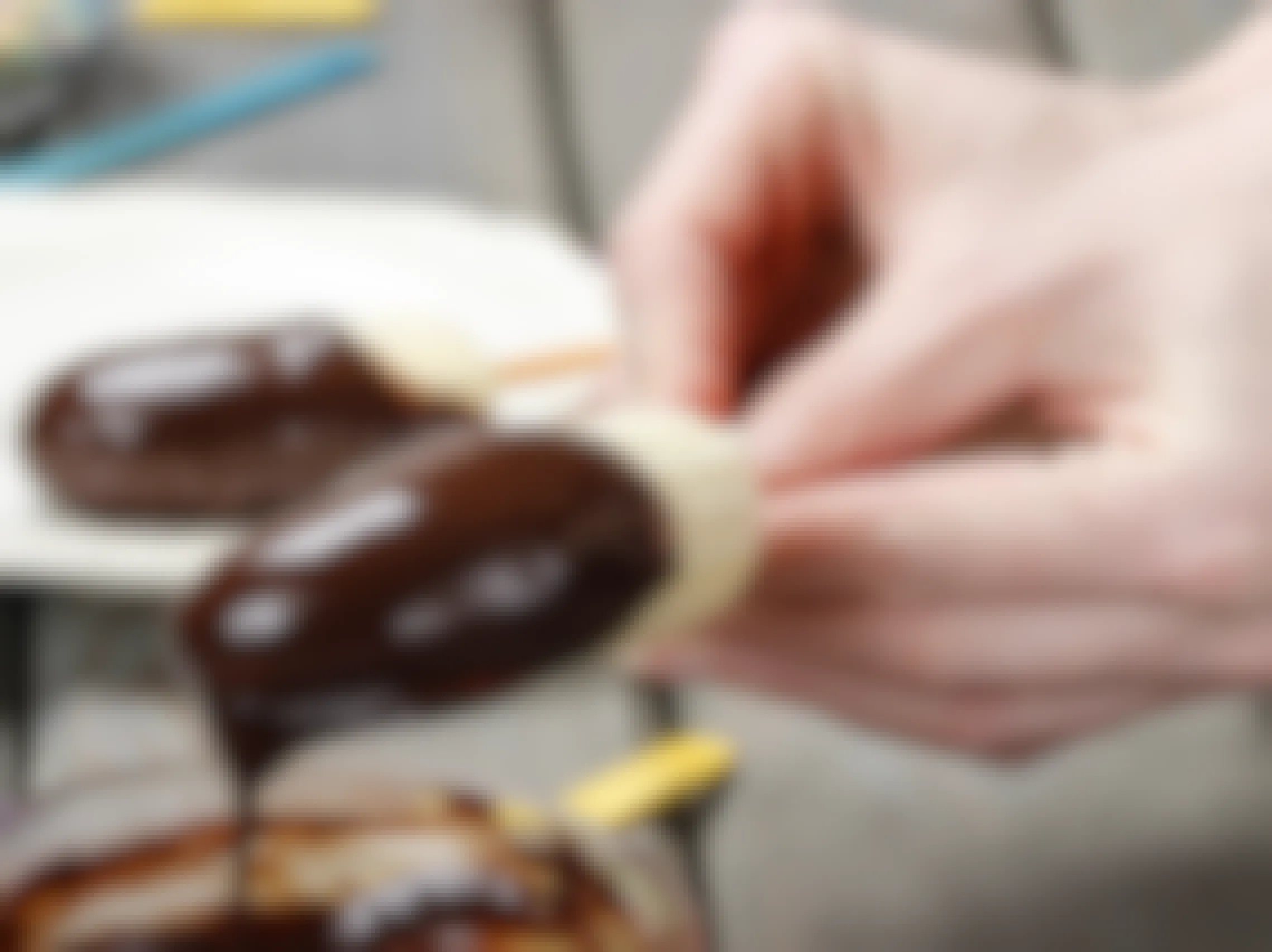 A person dipping a banana half on a popsicle stick into some melted chocolate.