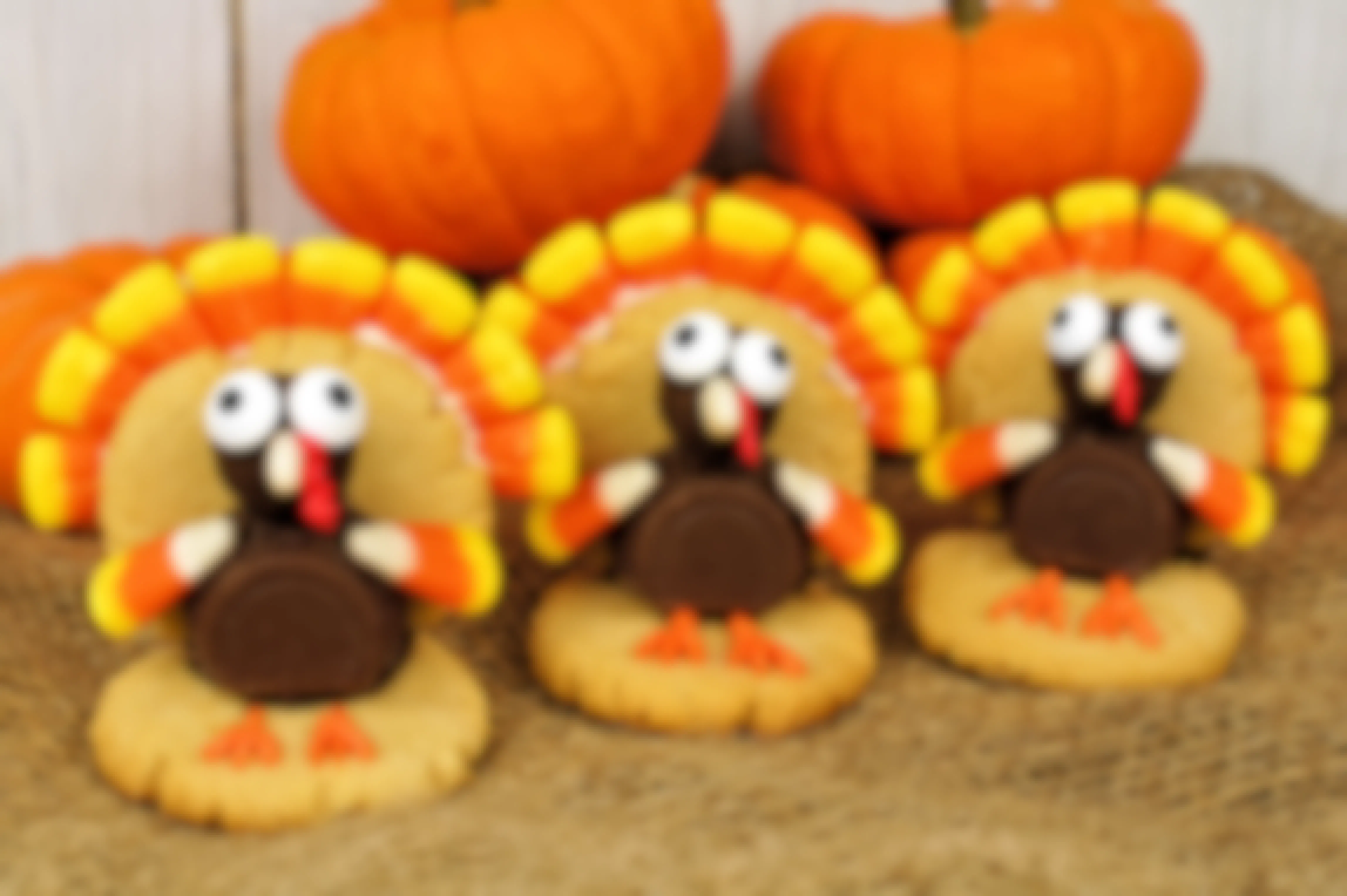 Three turkey-shaped cookies made with leftover Halloween candy on a table with some pumpkins.