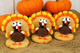 Three turkey-shaped cookies made with leftover Halloween candy on a table with some pumpkins.