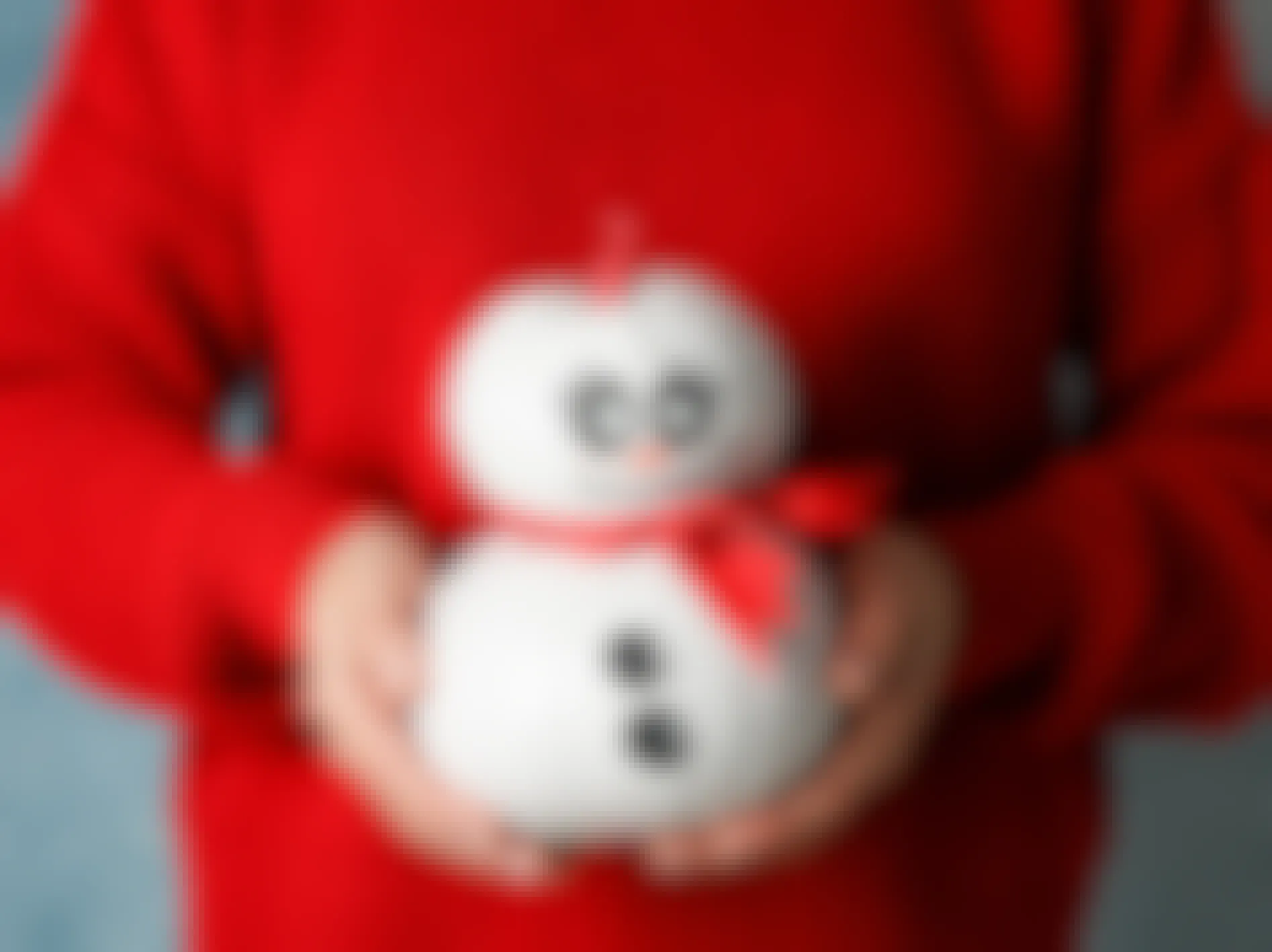 A person in a red sweater holding a snowman made from painted pumpkins.