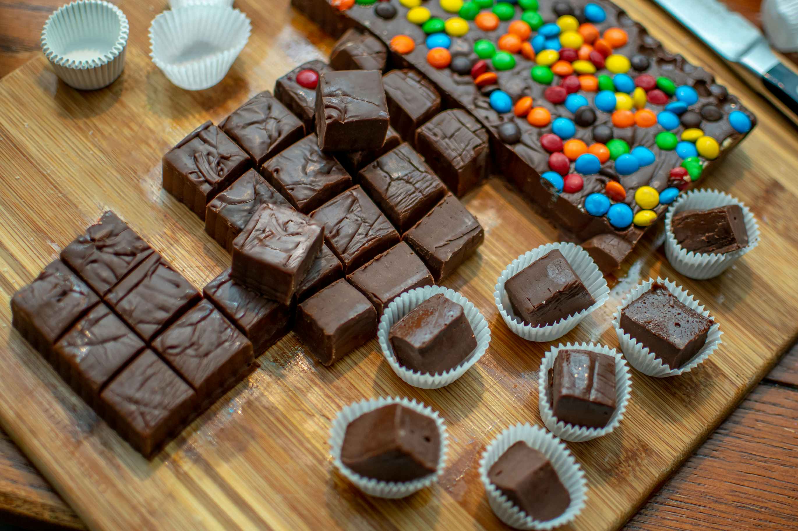 Some homemade chocolate fudge cut into squares next to another fudge with candies on top.