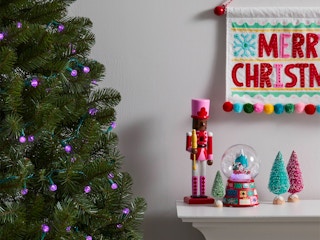 A Christmas tree decorated with purple string lights next to a mantle decorated for Christmas.