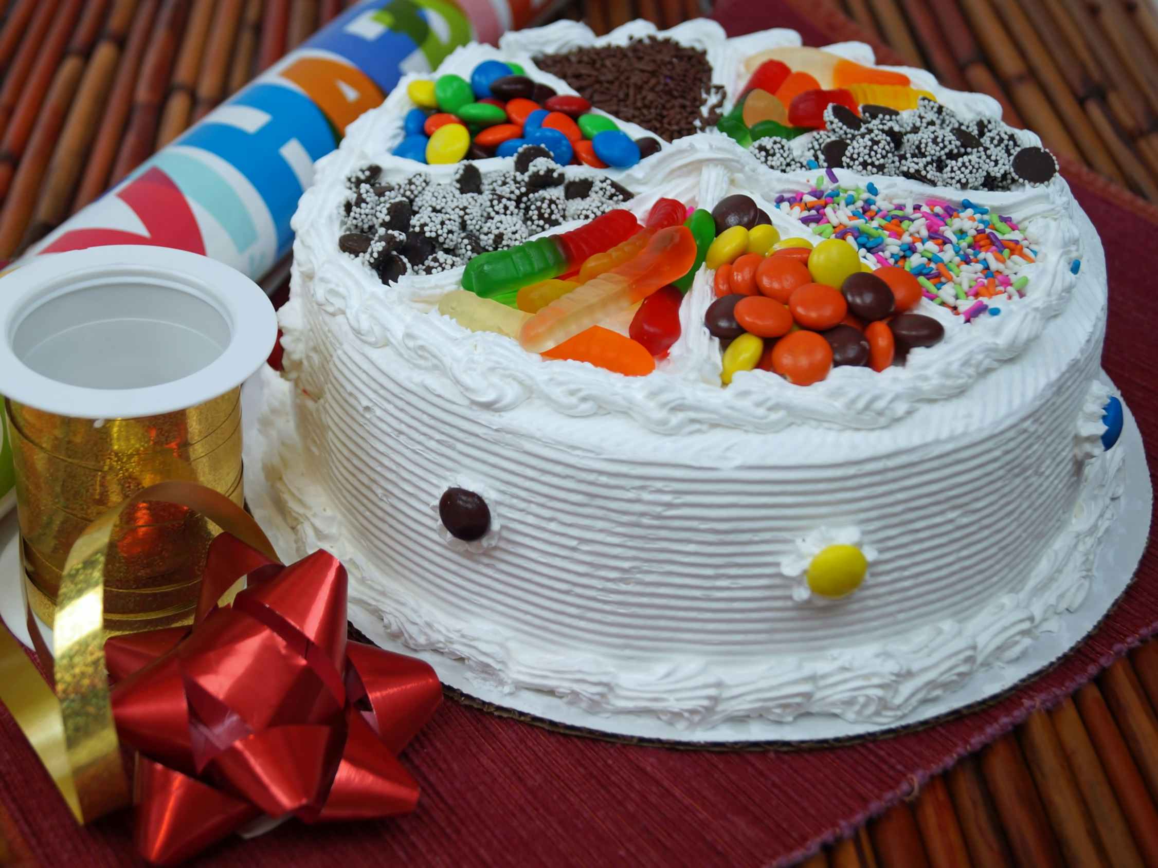 A cake topped with different kinds of candies sitting on a table next to a bow, some ribbon, and wrapping paper.