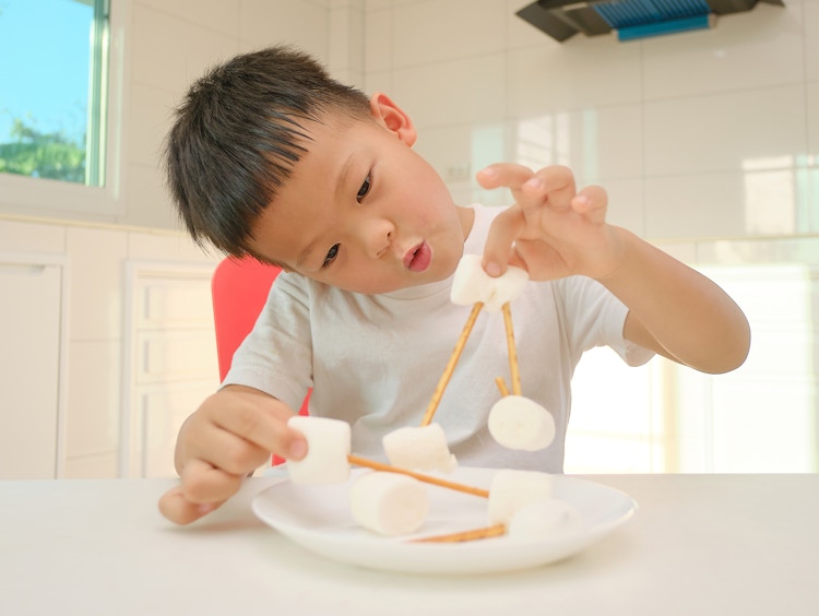 A little boy connecting marshmallows with sticks on a plate.