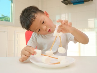 A little boy connecting marshmallows with sticks on a plate.