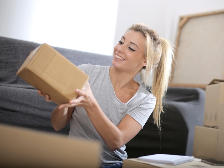 A college student looking at a box that was delivered to her and smiling.