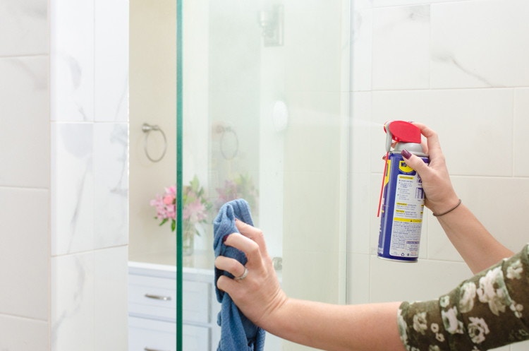 Person spraying WD-40 on a shower glass door