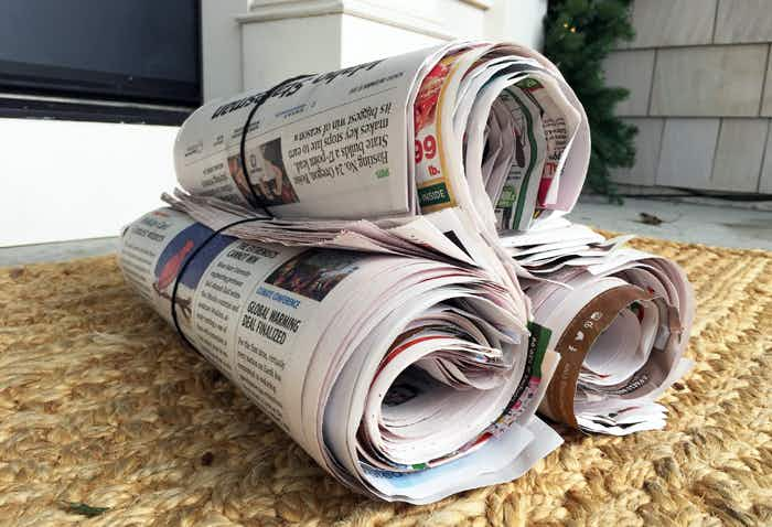 Rolled newspapers sitting on the ground in front of a door.