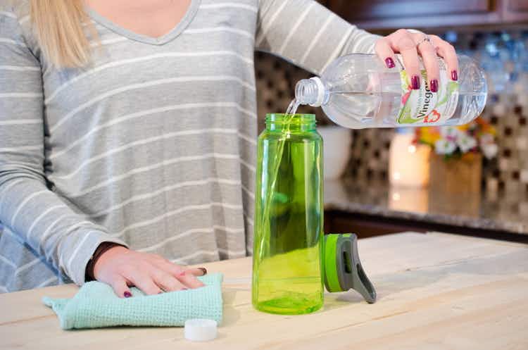 White vinegar being poured into a green plastic water bottle.