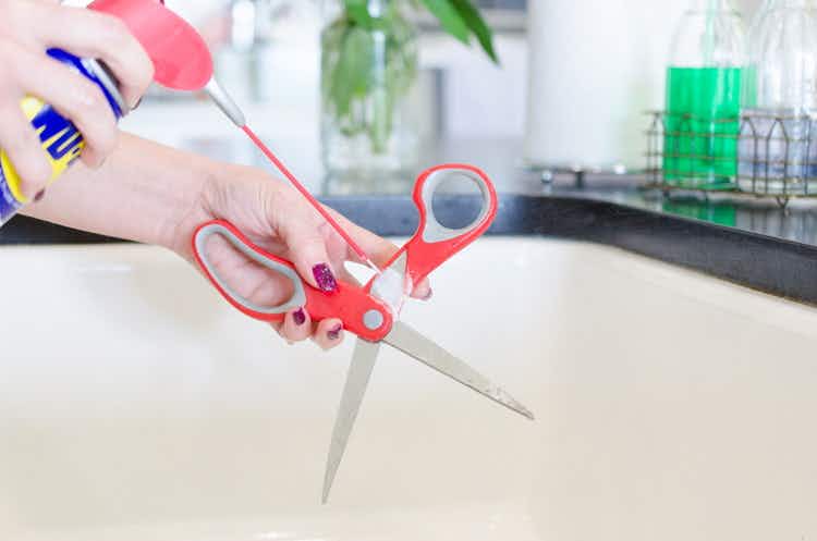 WD-40 being sprayed onto scissors near a sink